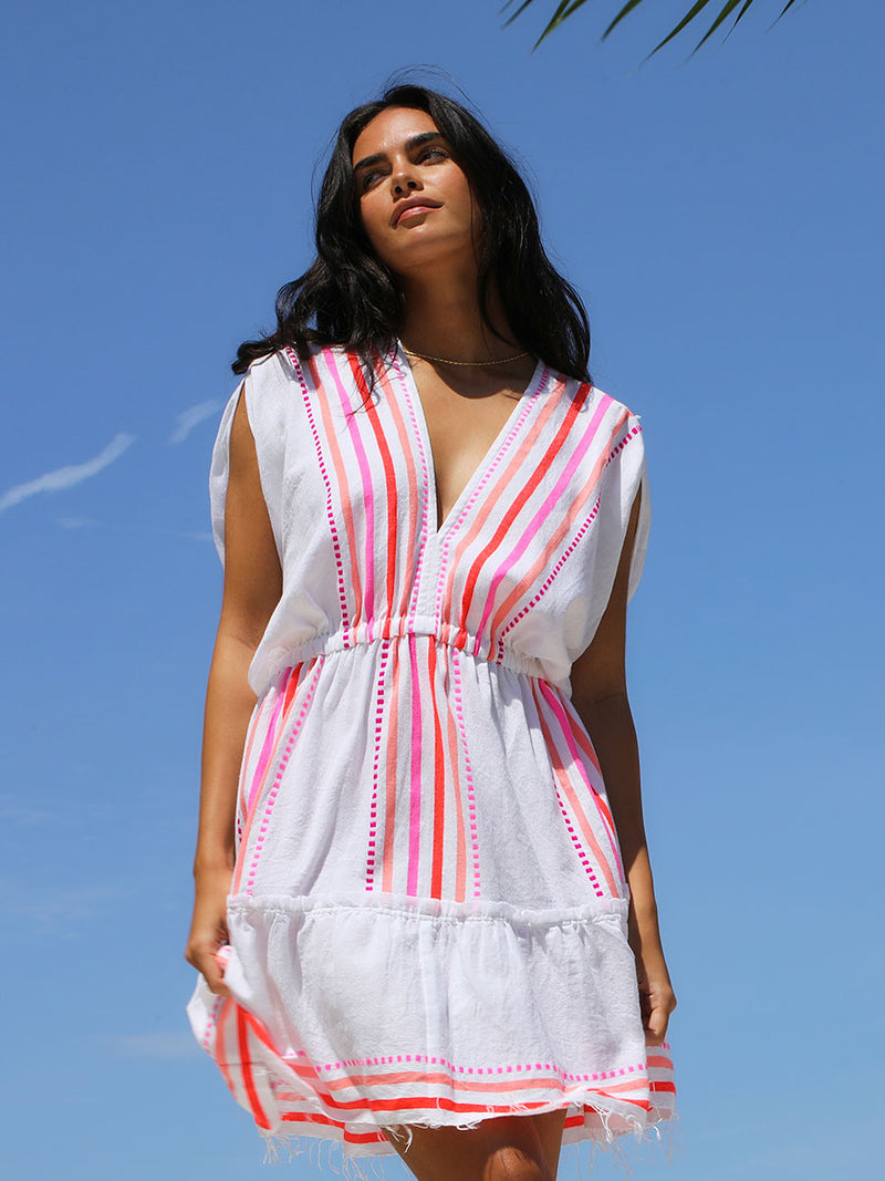 A woman standing wearing the Eshe Short Plunge Neck Dress in pink featuring pink stripes and dots pattern.