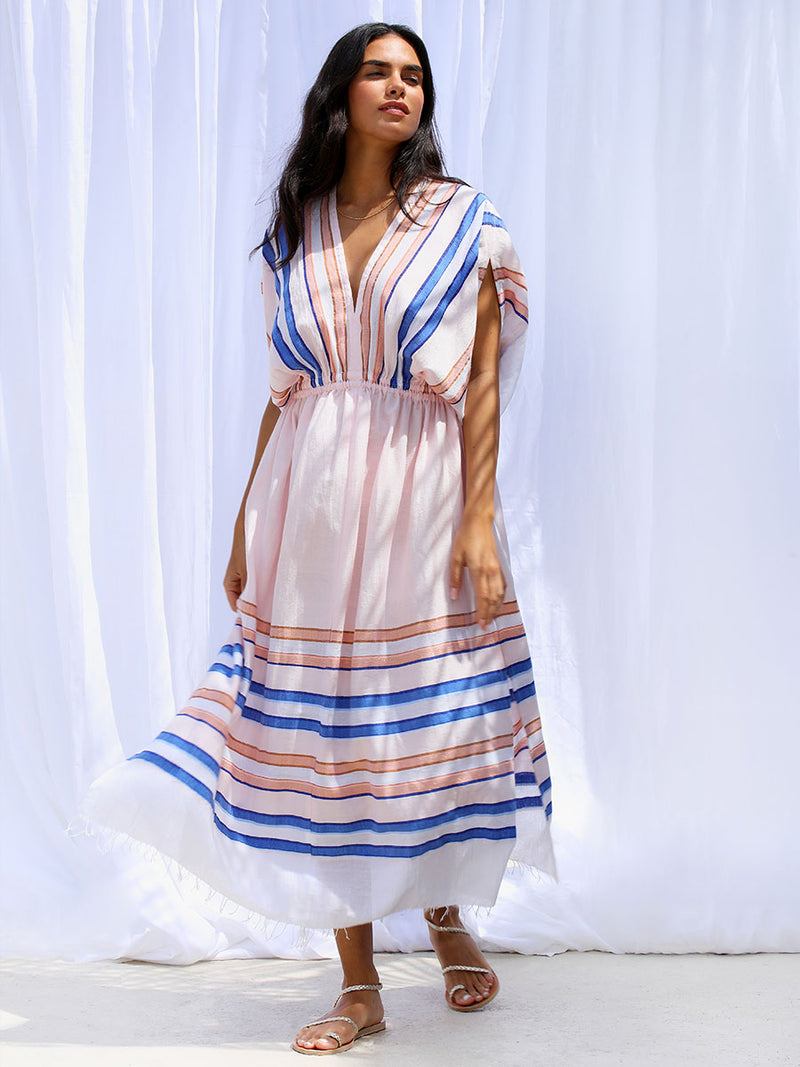 The view of a woman wearing the Eskedar Plunge Neck Dress in Seashell featuring blue, white, brown, nude and gold lurex stripes