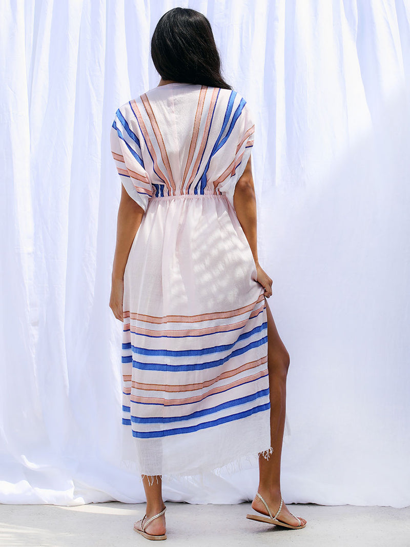 The back view of a woman wearing the Eskedar Plunge Neck Dress in Seashell featuring blue, white, brown, nude and gold lurex stripes