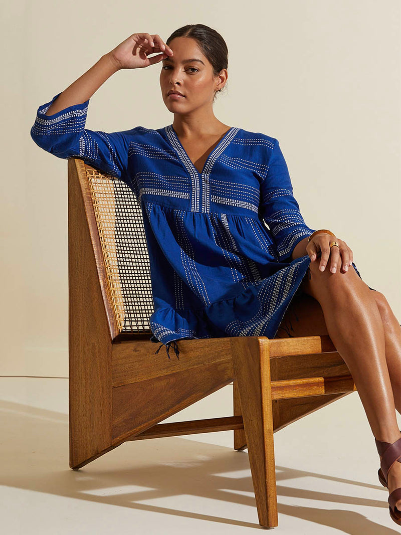 Woman sitting wearing the Inku Flutter Dress featuring textured white dots on deep blue background.