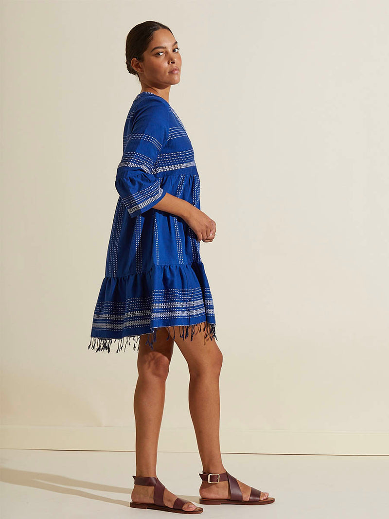 Side view of a woman standing wearing the Inku Flutter Dress featuring textured white dots on deep blue background.