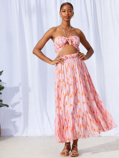 A woman standing with her hands on her hips wearing the Gigi Cutout Dress in Multi Pink featuring pink, peach and orange allover chevron print and strips of gold lurex. 