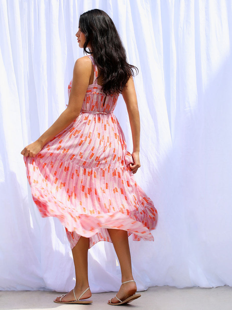 A back view of a woman walking wearing the Gigi Sweepy Sundress in Multi Pink featuring pink, peach and orange allover chevron print and strips of gold lurex.