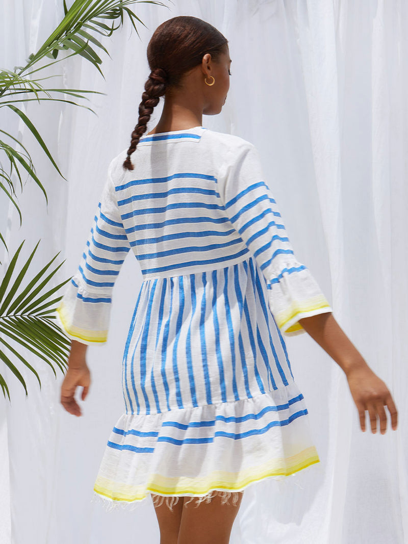 A back view of a woman standing wearing the Hirut Flutter Dress in Blue featuring blue stripes on white foreground and yellow degrade stripes at the edges.