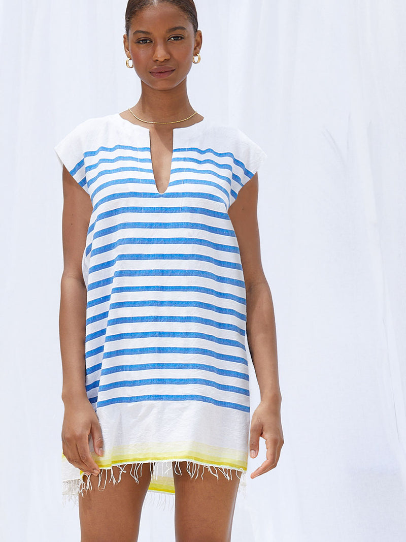 Woman standing wearing  the Hirut Tunic Dress in Blue featuring blue stripes on white foreground and yellow degrade stripes at the bottom hem.