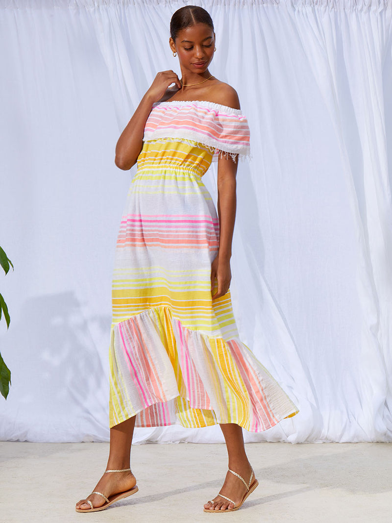 A view of a woman walking wearing the Jamila Beach Dress featuring shades of yellow and pink stripes on white foreground.