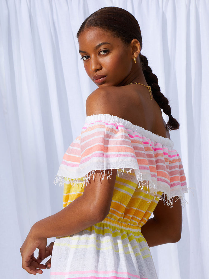 A close up of the side view of a woman wearing the Jamila Beach Dress featuring shades of yellow and pink stripes on white foreground.