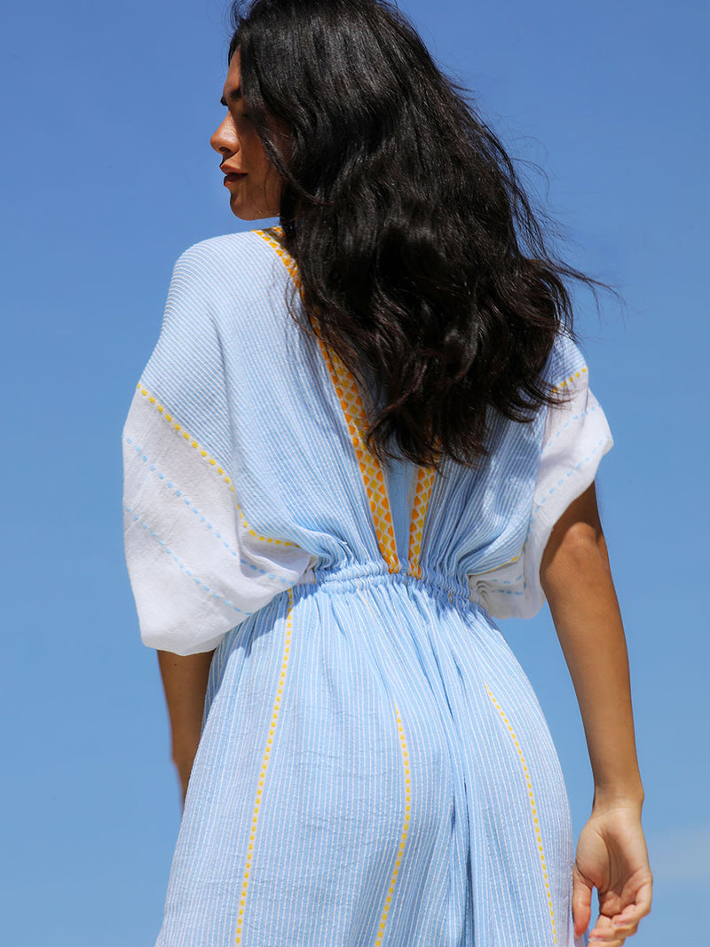 The back view of a woman wearing the Jemari Plunge Neck Dress in sky blue featuring yellow and orange diamond patterns
