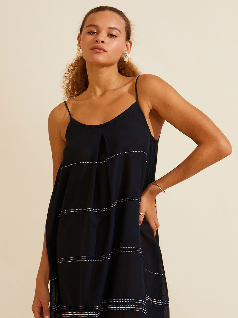 A woman standing with her hand on her hip wearing the Leliti Slip Dress in Black with white stitching allover.