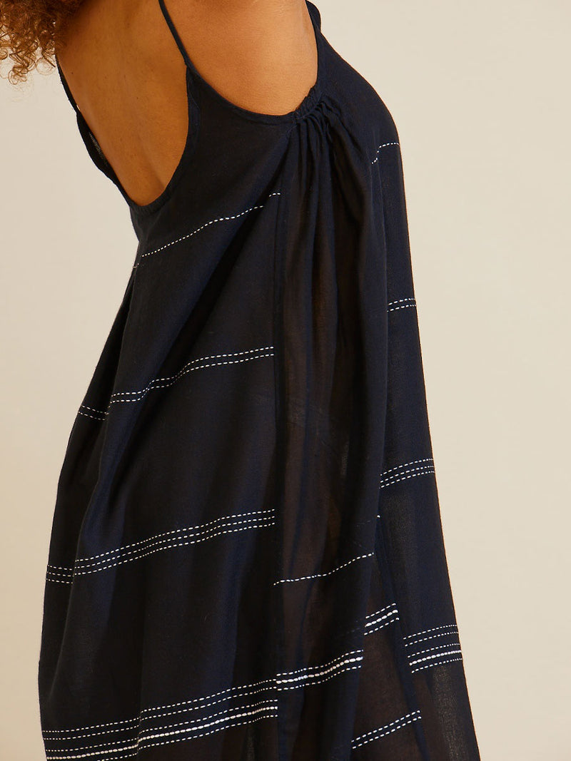 Close up side view a woman standing with her arms up in the airwearing the Leliti Slip Dress in Black with white stitching allover.