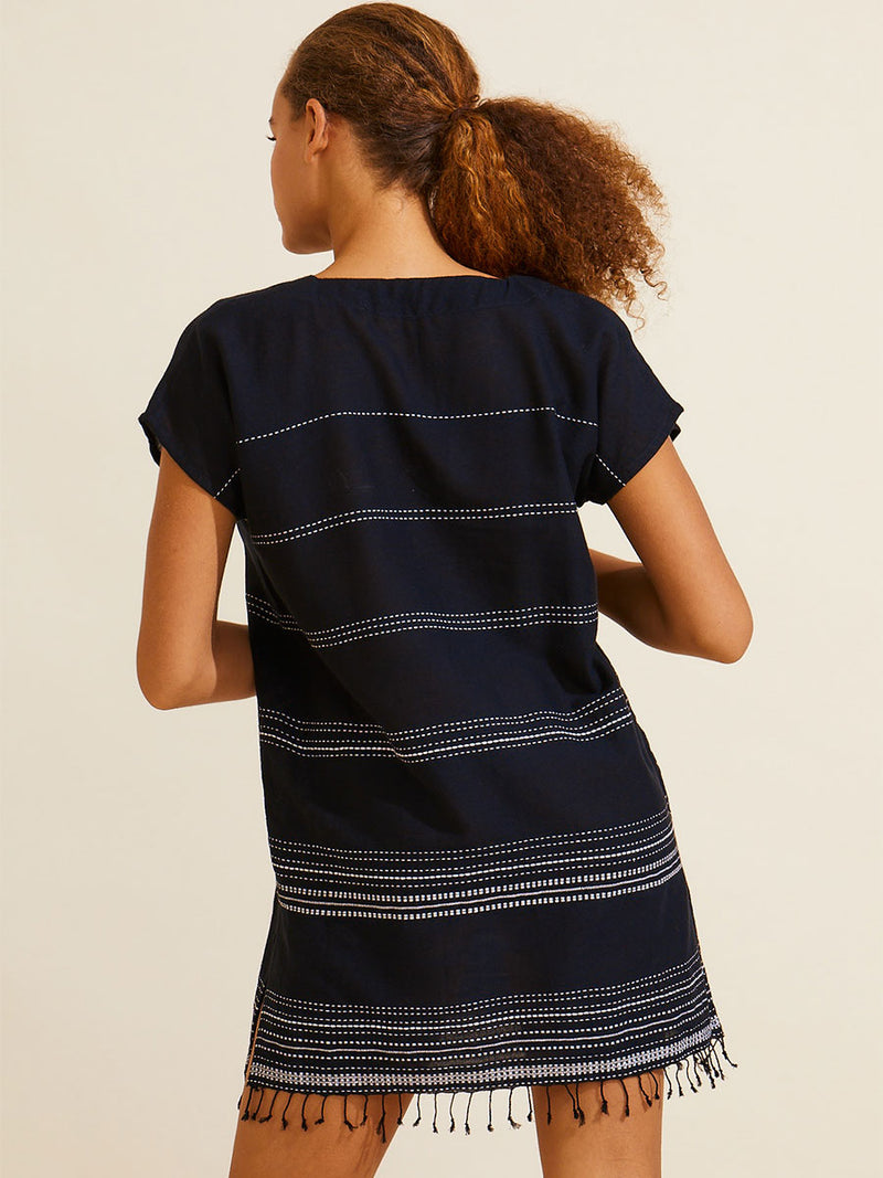 Back view of a woman standing wearing the Leliti Tunic Dress in Black with white stitching allover.
