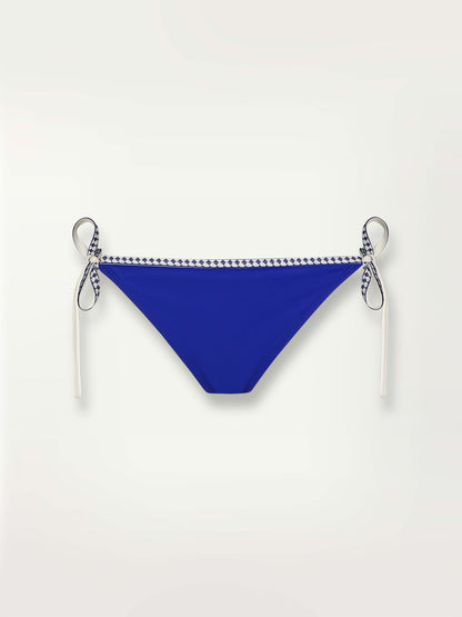 Product shot of the Lena String Bikini Bottom  in bright neon blue adorned with navy and white diamond jacquard pattern on the trims