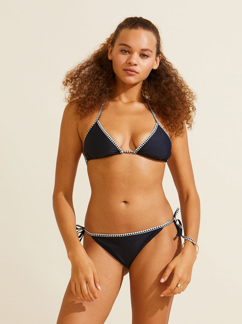 Woman standing wearing the Sofia Triangle Top and matching string bikini in Black featuring black and white tibeb trim.