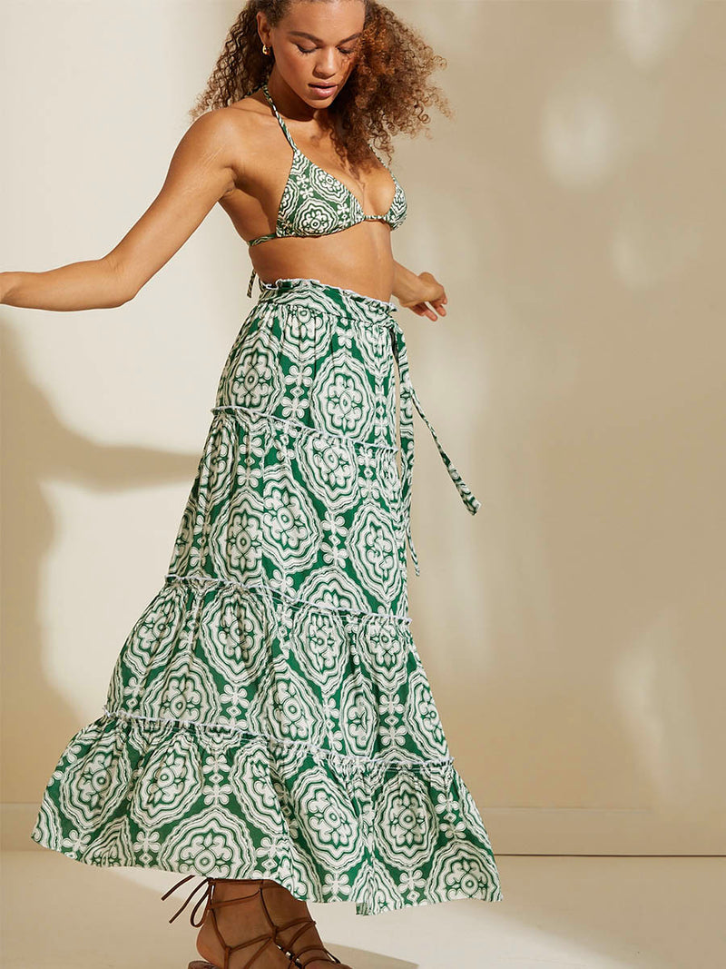 Woman twirling wearing the Medallion Maxi Skirt and Triangle Bikini Top featuring architectural white patterns on a deep green background.