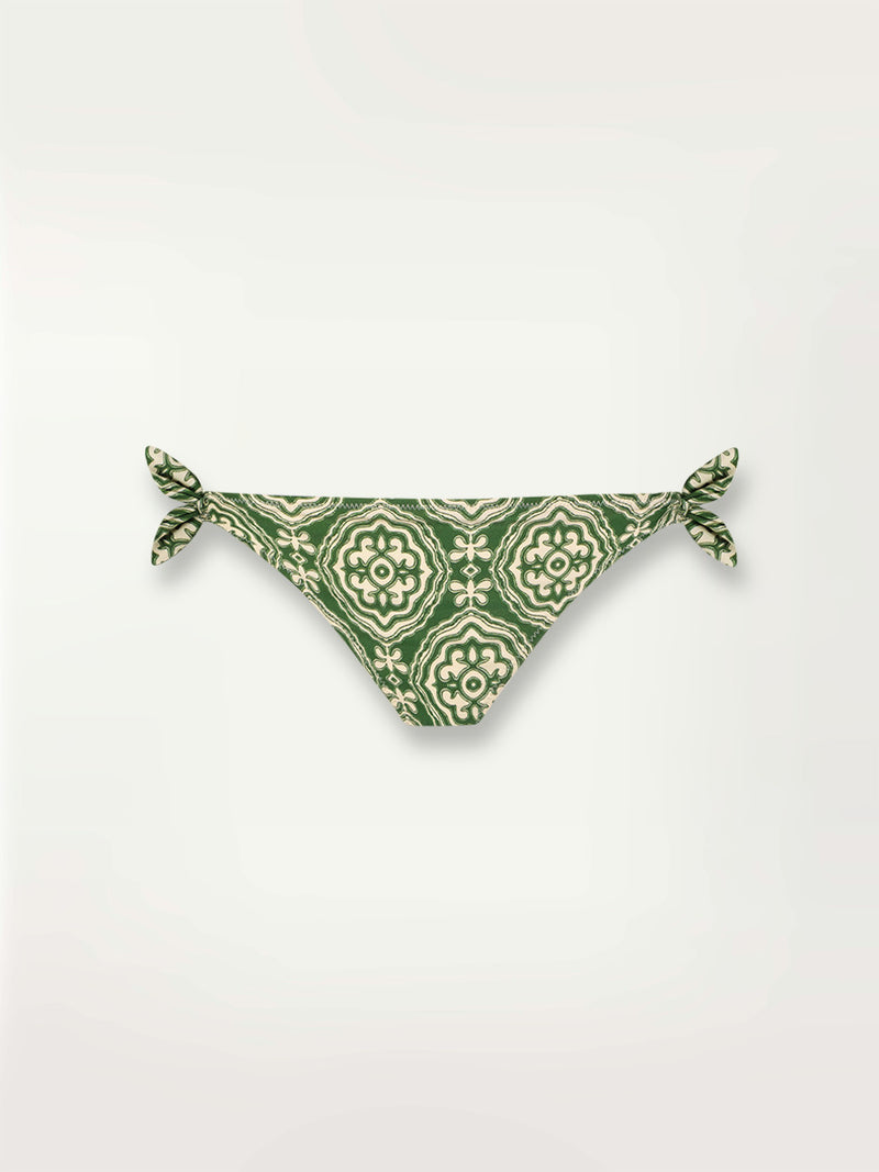Product shot of the Medallion Side Tie Bikini Bottom featuring architectural white patterns on a deep green background.