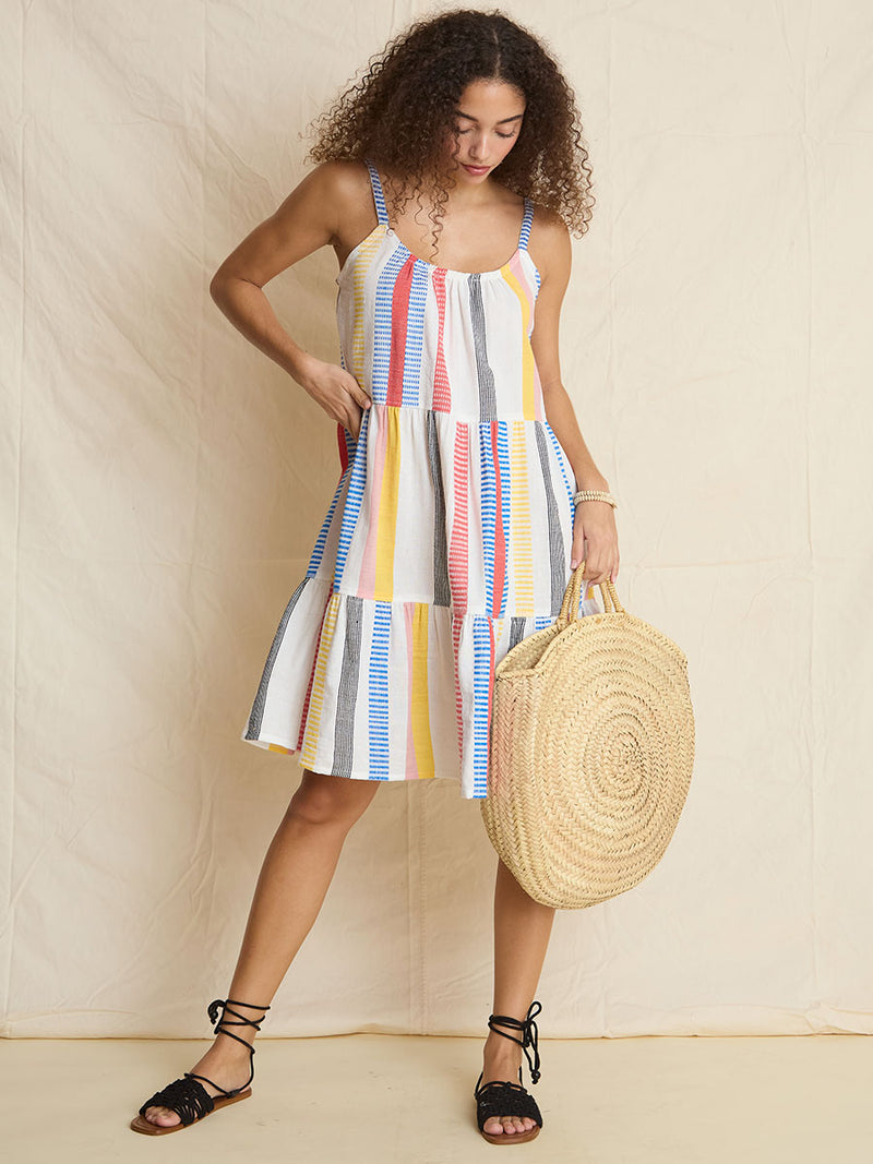 A woman standing wearing the Meseret Midi Cascade Dress featuring a variety of pink, yellow, black, red, and blue stripe patterns. 