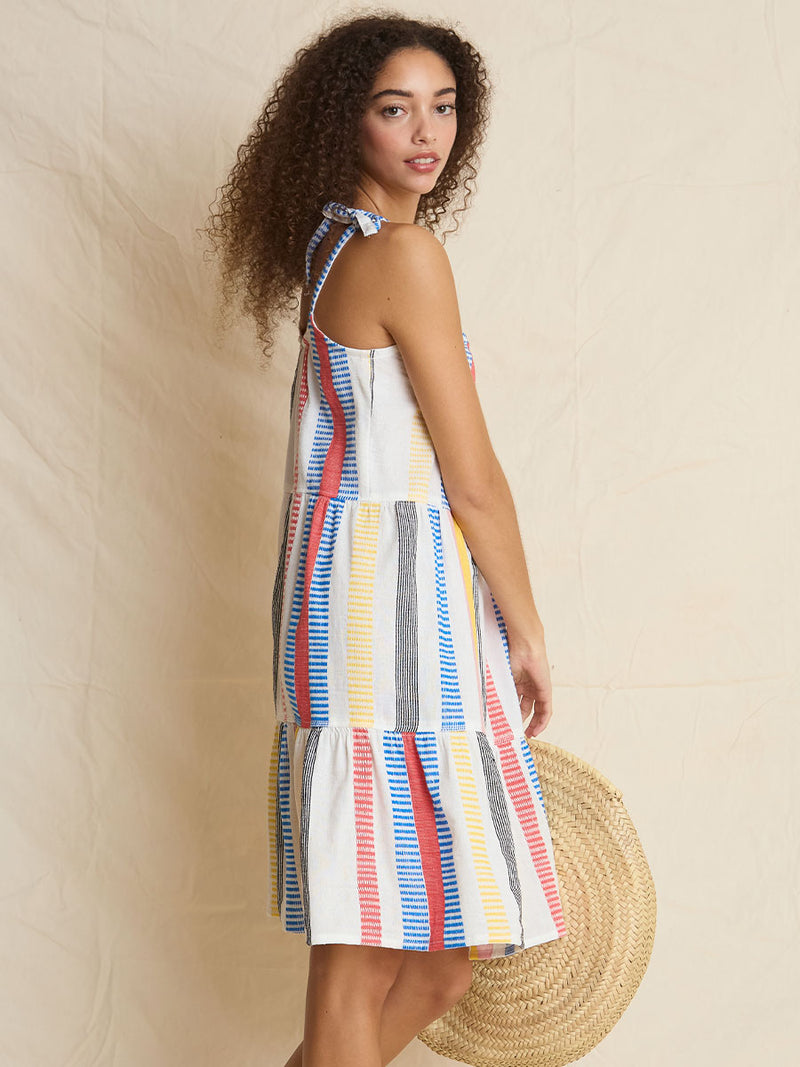 The side view of a woman standing wearing the Meseret Midi Cascade Dress featuring a variety of pink, yellow, black, red, and blue stripe patterns. 