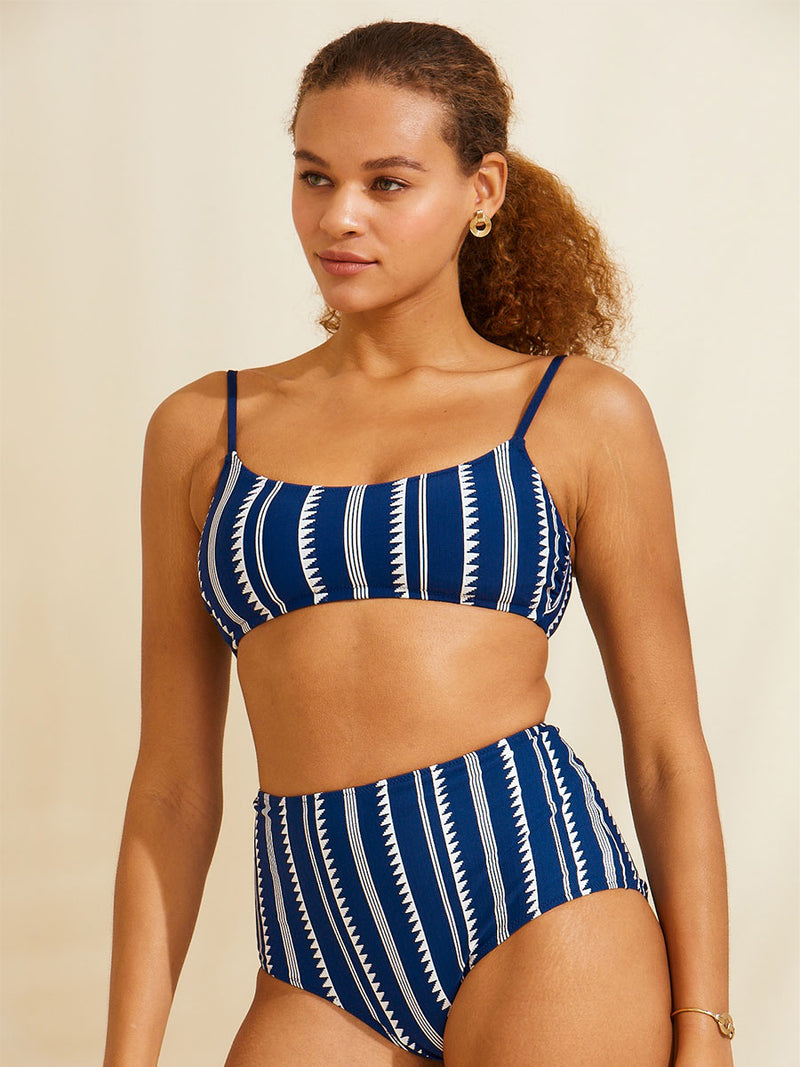 Woman standing wearing a navy Nunu bralette bikini top and matching high waist bikini bottom with white triangles and stripes
