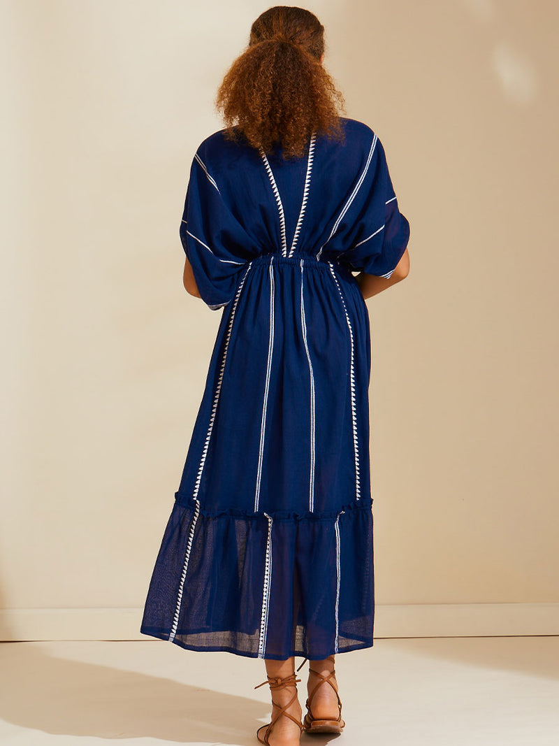 Back view of a woman standing wearing  the Nunu Plunge Neck dress in navy blue featuring a navy with white vertical stripes and graphic lines.
