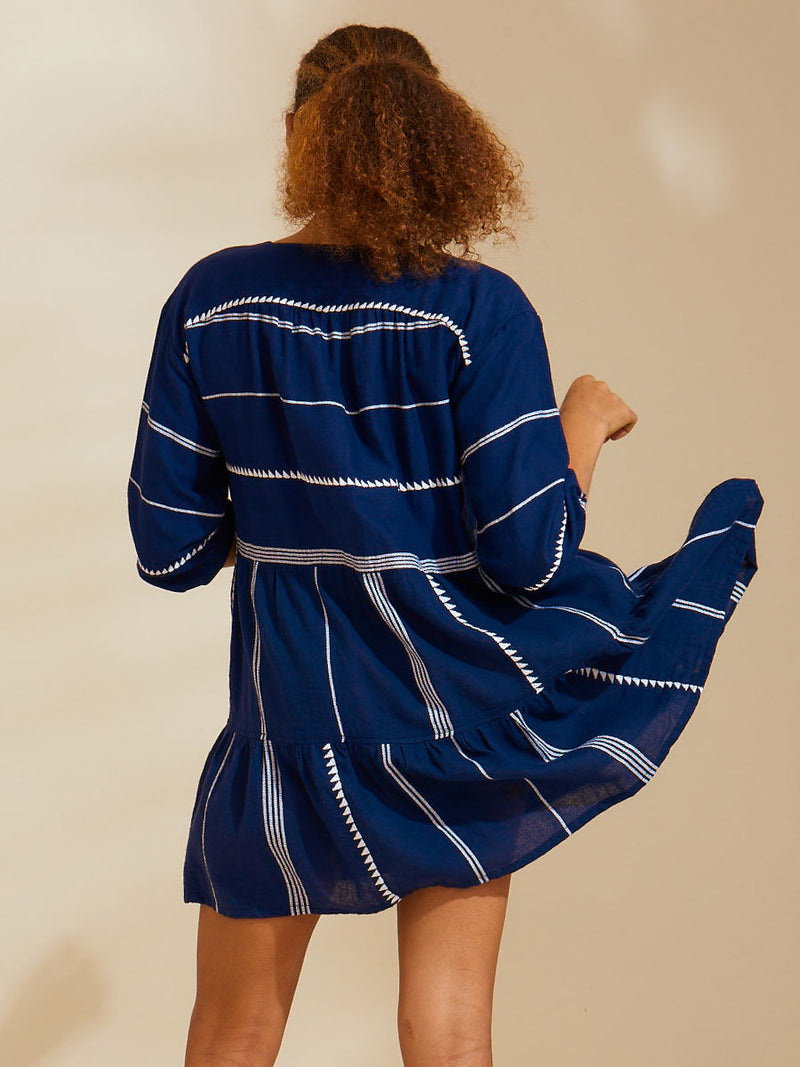 Side view of a woman standing wearing navy Nunu short popover dress with white triangles and stripes