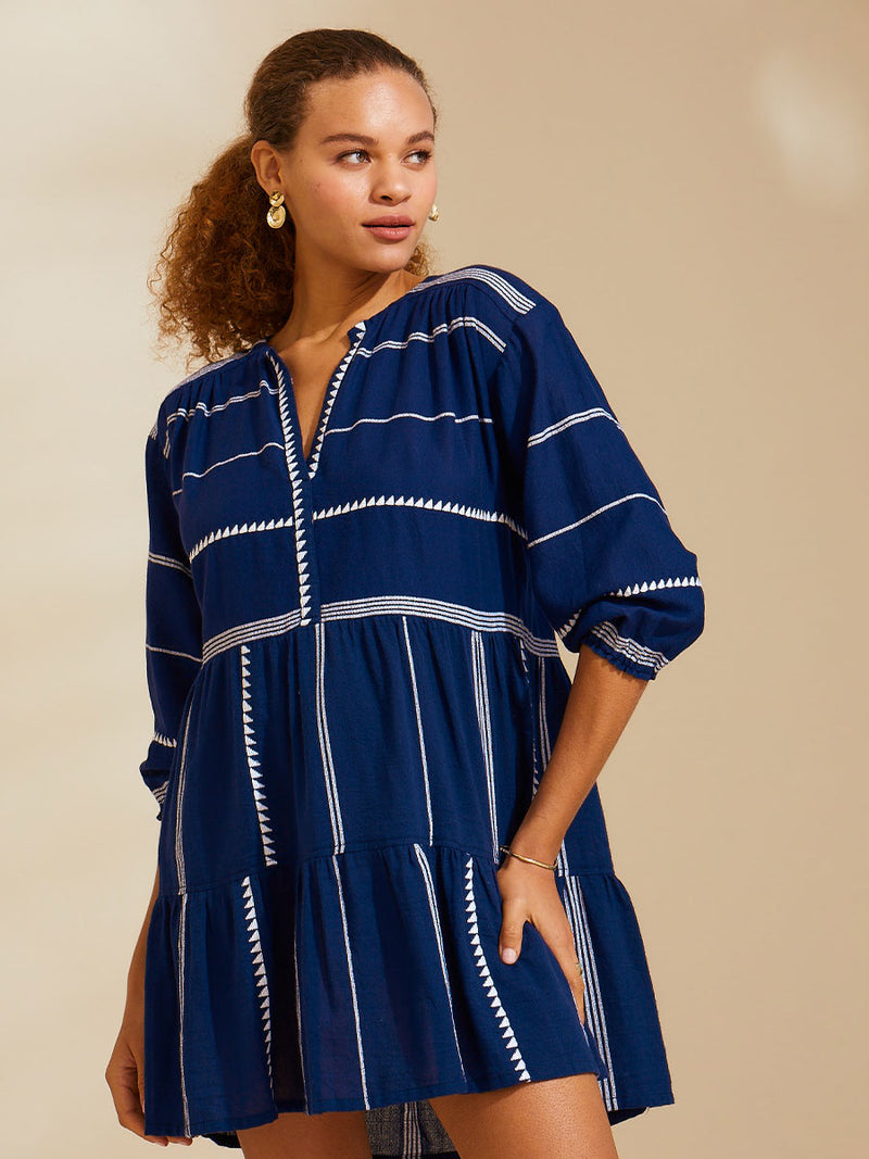 Woman standing with her hand on her leg wearing navy Nunu short popover dress with white triangles and stripes