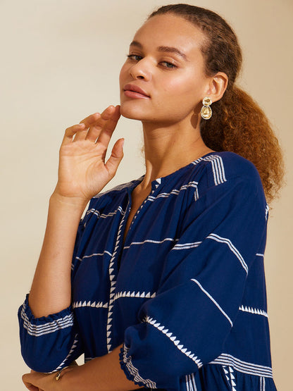 Close up view of a woman with her hand touching her face wearing navy Nunu short popover dress with white triangles and stripes