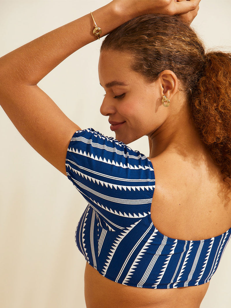 Side view of woman standing with her arms over her head wearing a navy Nunu pouf swim top with white triangles and stripes with matching high waist bottom