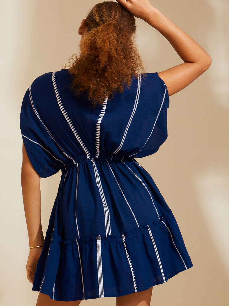 Back view of a woman standing with her hand on her head wearing the Nunu short Plunge Neck in Navy blue with white stripes and graphic lines.