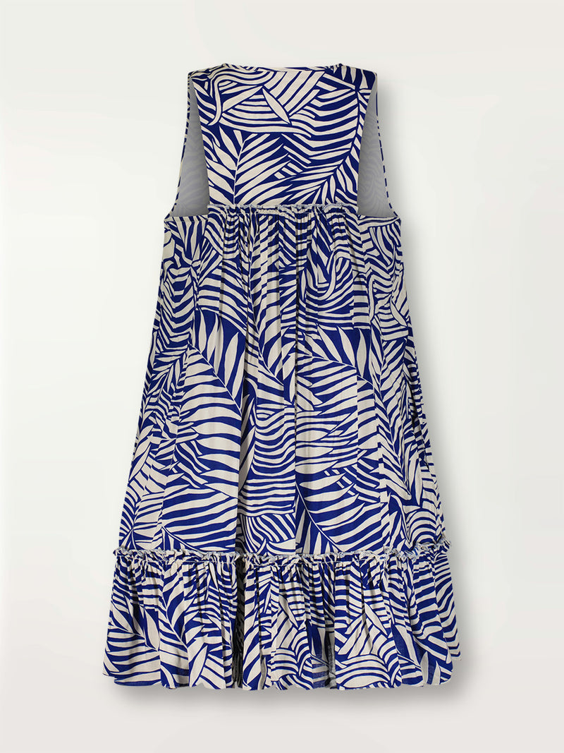 Product shot of the back the Palm Leaf Bib Dress featuring palm tree patterns on a rich blue background.