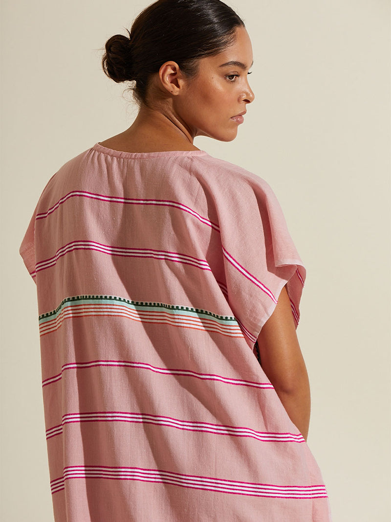 Back view of a woman wearing the Rosa Classic Caftan featuring architectural details and geometric border patterns woven on a soft pink background.