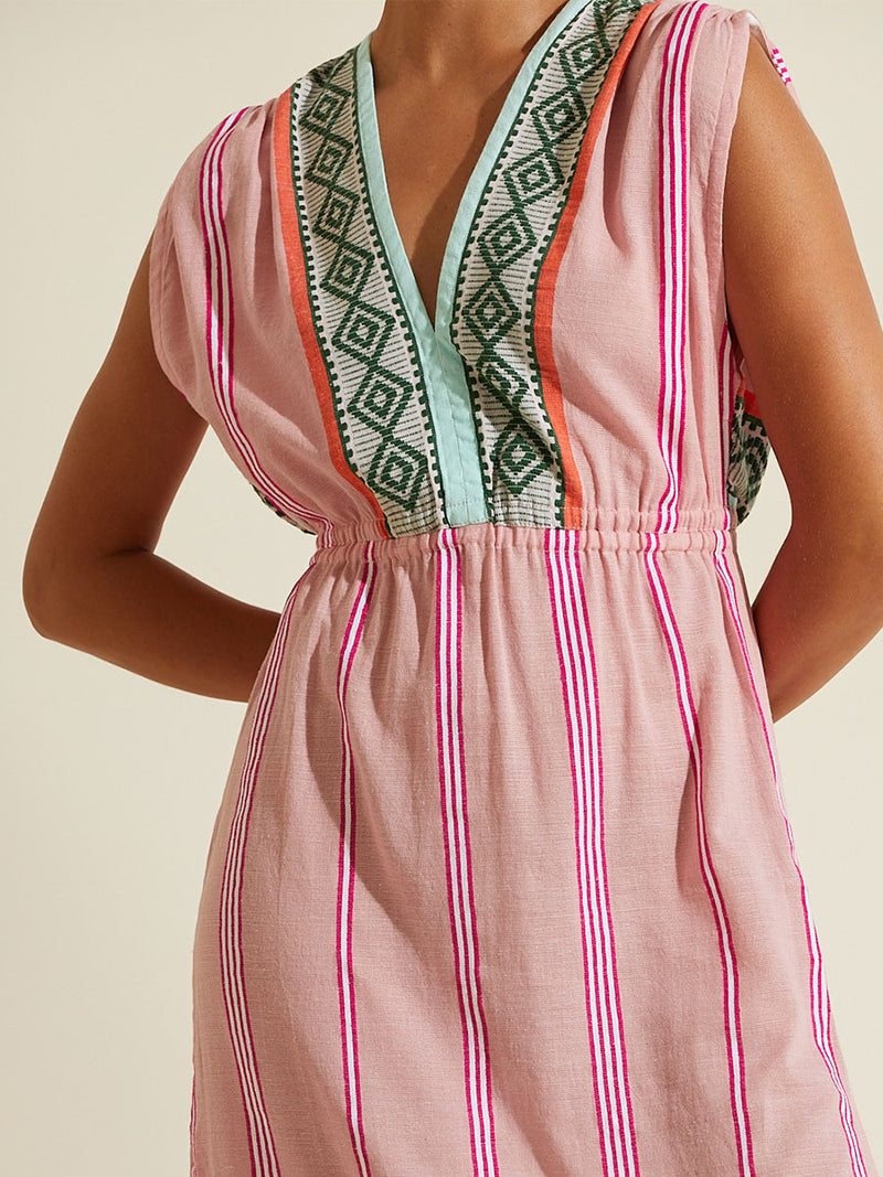 Close up on the chest of a woman wearing the Rosa Sleeveless Plunge Neck Dress featuring architectural details and geometric border patterns woven on a soft pink background.