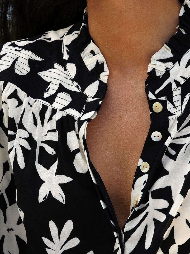 A close up of the neckline of the Sea Floral Ruffle Blouse in Black featuring white allover floral print.