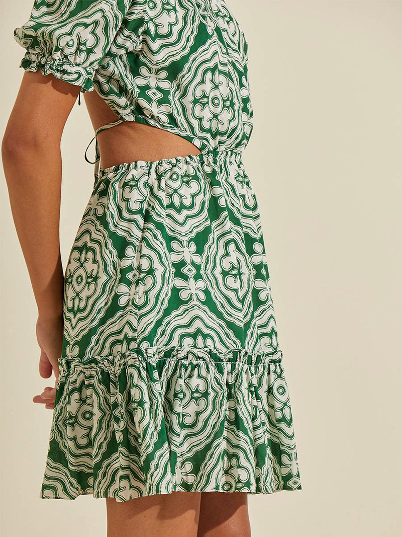 Side view of a woman wearing the Medallion Short Open Back Dress featuring architectural white patterns on a deep green background.