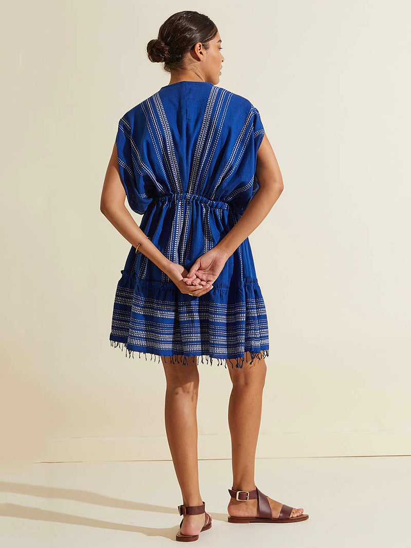 Back view of a woman standing wearing the Inku Short Plunge Neck Dress featuring textured white dots on deep blue background.