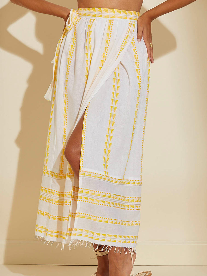 Close up on the legs of a woman wearing the Abeba Wrap Skirt featuring the yellow signature Tibeb pattern and gold lurex highlights on a white background.