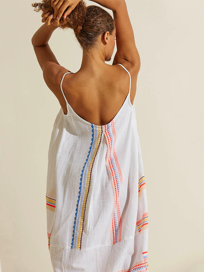 Back view of a woman standing with her hands over her headwearing the Bekah Slip Dress featuring 10 tutti frutti colors embroidered on a white background.  