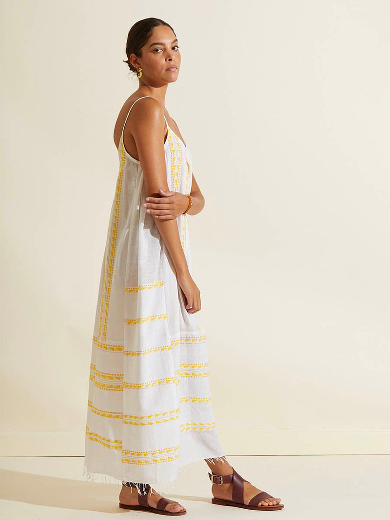 Side view of a woman standing wearing the Abeba Slip Dress featuring the yellow signature Tibeb pattern and gold lurex highlights on a white background.