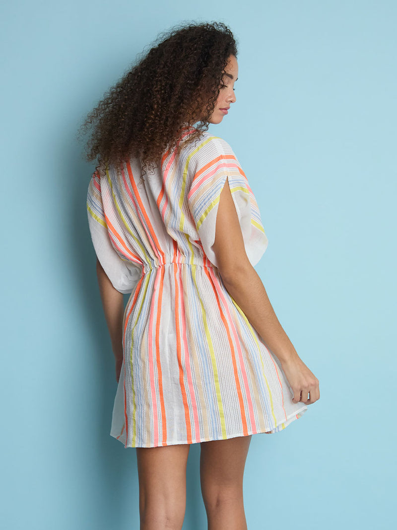 The back view of a woman standing wearing the Tirunesh Short Plunge Neck Dress featuring pale pink, blue, yellow, orange and nude stripes