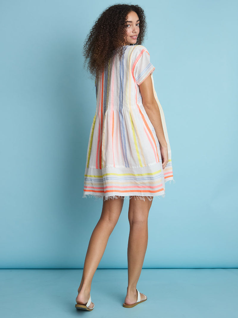 The back view of a woman standing wearing the Tirunesh Smock Dress featuring pale pink, blue, yellow, orange and nude stripes.