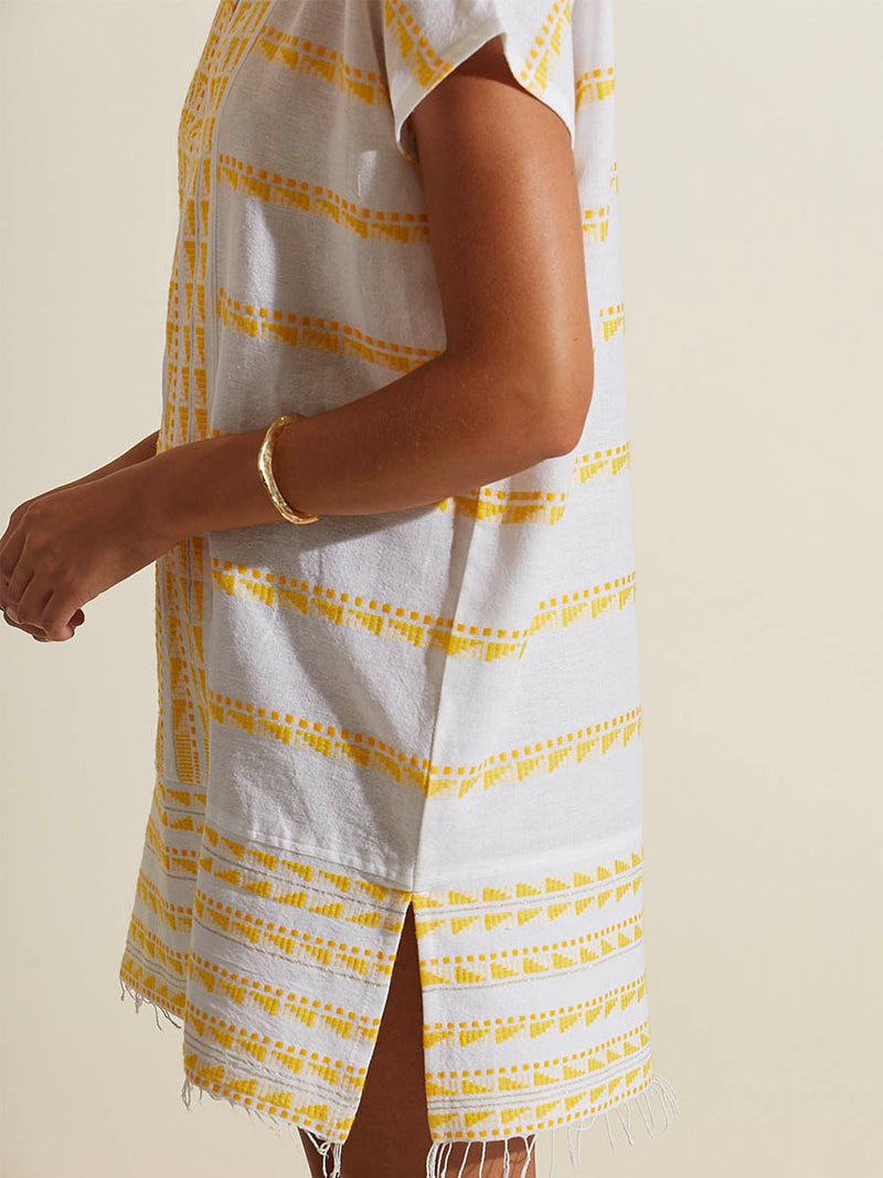 Side view of a woman wearing the Abeba Tunic Dress featuring the yellow signature Tibeb pattern and gold lurex highlights on a white background.