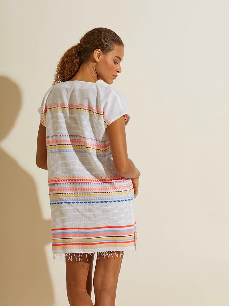 Back view of a woman standing wearing the Bekah Tunic Dress featuring 10 tutti frutti colors embroidered on a white background.  