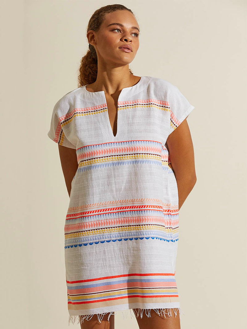 Woman standing with her hands in her back wearing the Bekah Tunic Dress featuring 10 tutti frutti colors embroidered on a white background.  