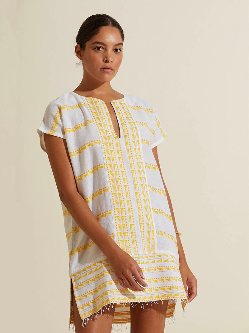 Woman standing wearing the Abeba Tunic Dress featuring the yellow signature Tibeb pattern and gold lurex highlights on a white background.