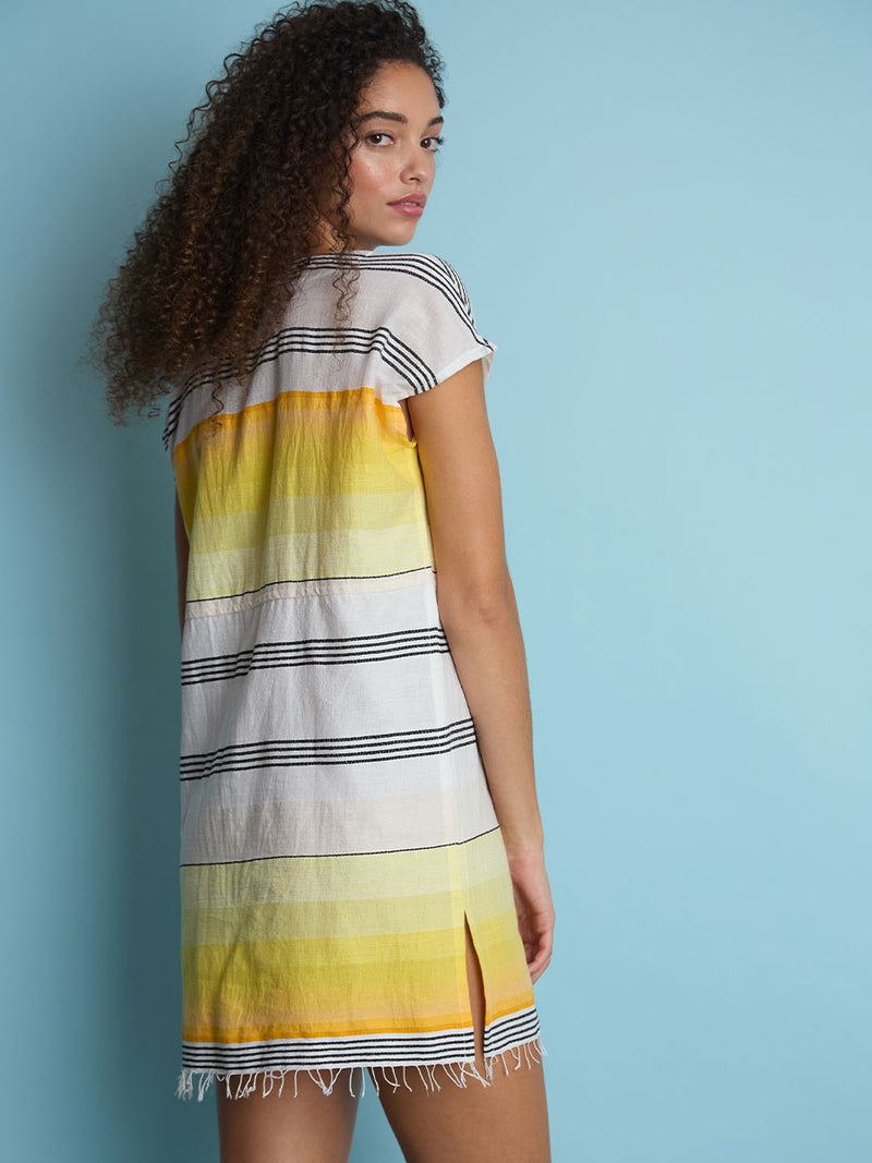 The back view of a woman standing wearing the Zena Tunic Dress in yellow featuring black stripes and yellow degrade.