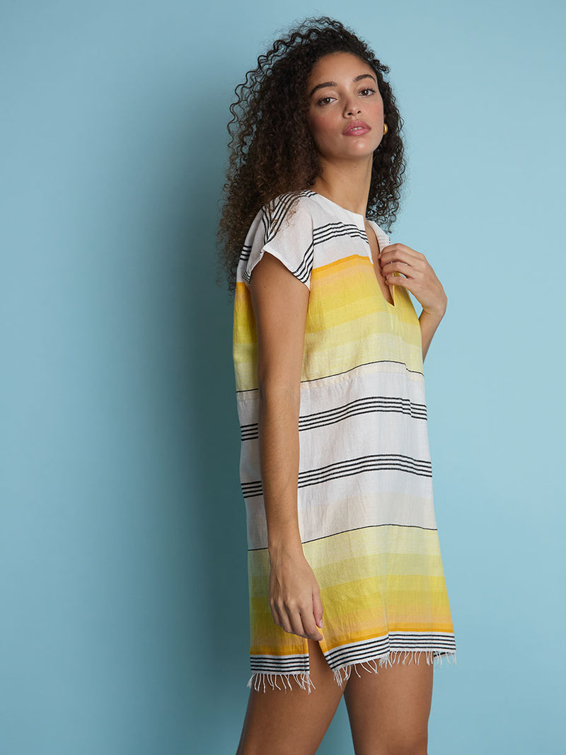 The side view of a woman standing wearing the Zena Tunic Dress in yellow featuring black stripes and yellow degrade.