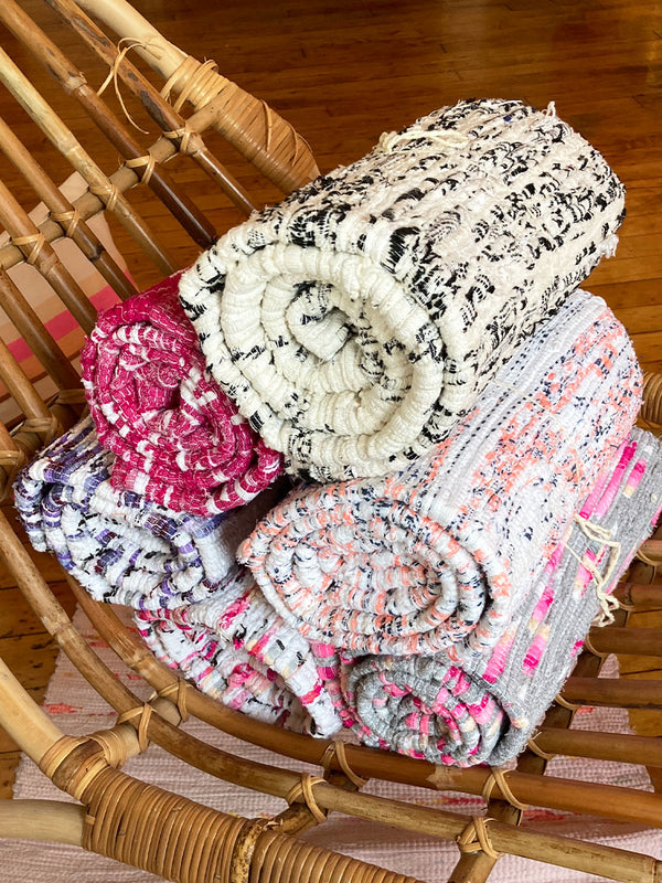 Several multi-colored handwoven rugs, rolled up and stacked in a pile on a wooden lounge chair.
